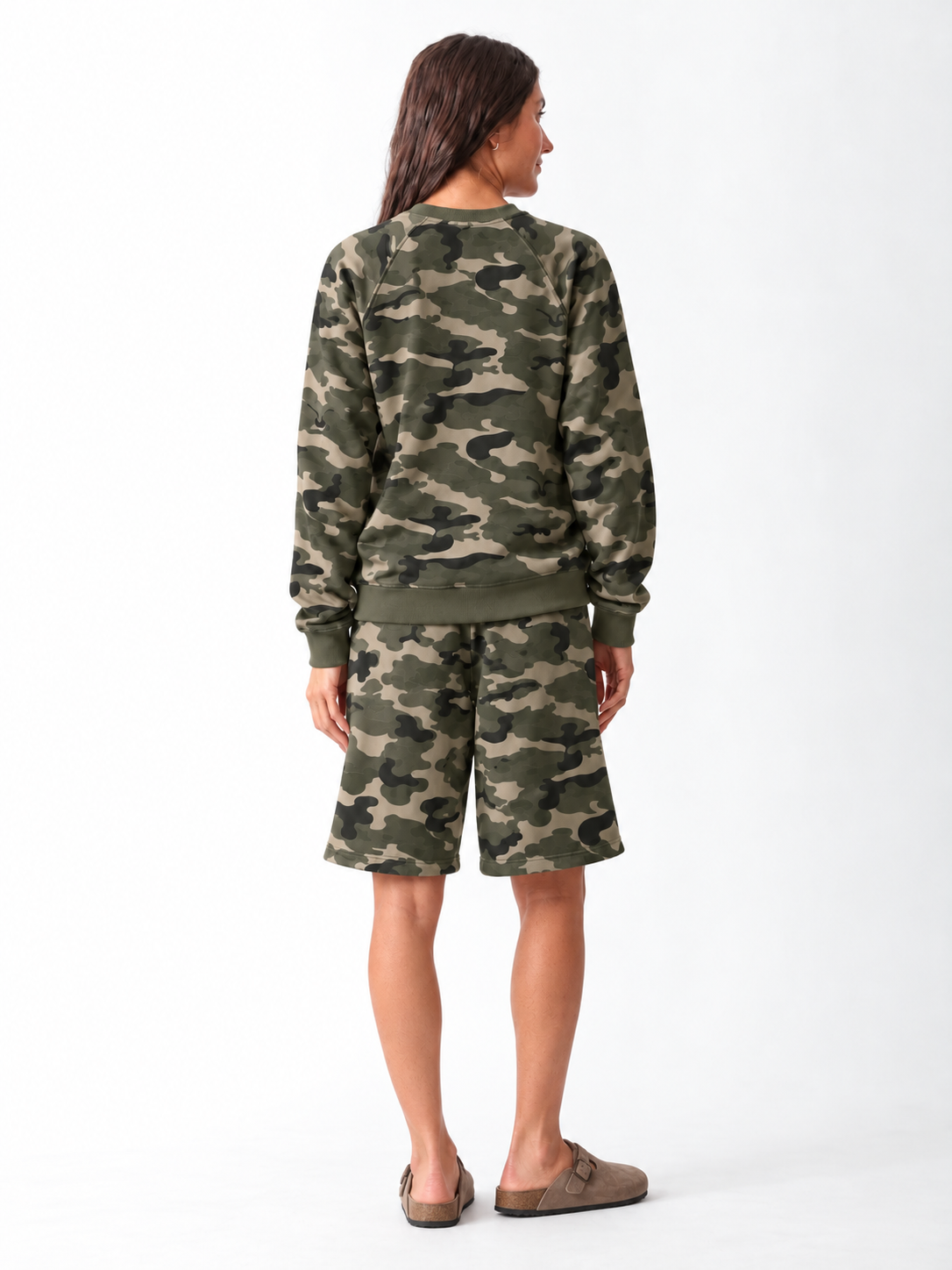 Model wearing a matching green camo set: a relaxed raglan-sleeve crewneck sweatshirt with ribbed cuffs and hem, and knee-length drawstring sweat shorts, styled with taupe suede clogs.
